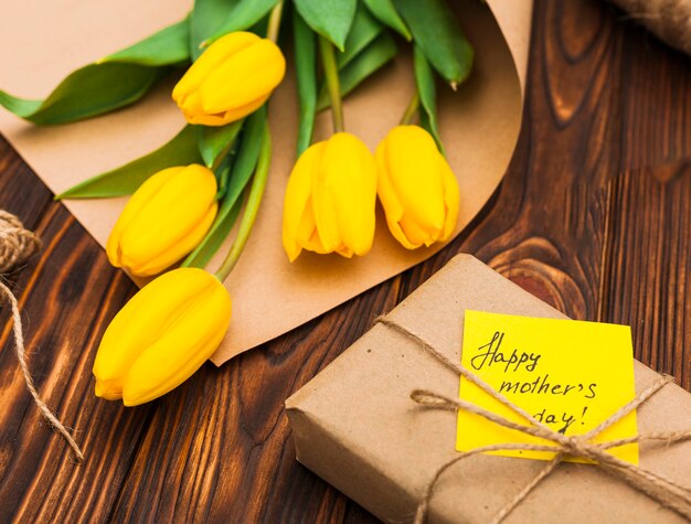 Inscripción del día de las madres felices con tulipanes amarillos y regalo