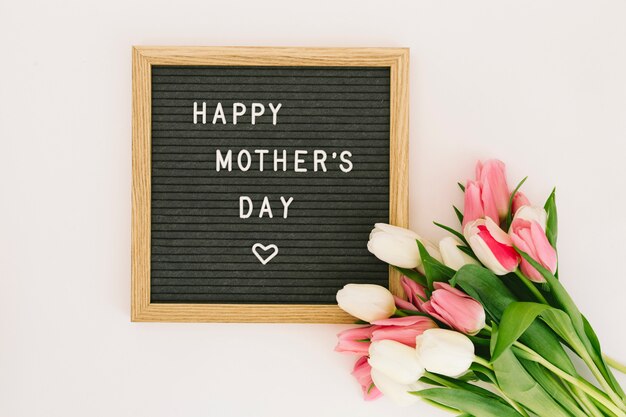 Inscripción feliz del día de madres a bordo con los tulipanes rosados