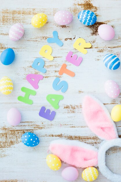 Inscripción feliz de Pascua con huevos de colores y orejas de conejo