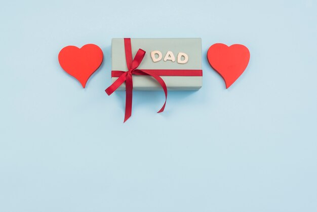 Inscripción de papá con caja de regalo y corazones en mesa