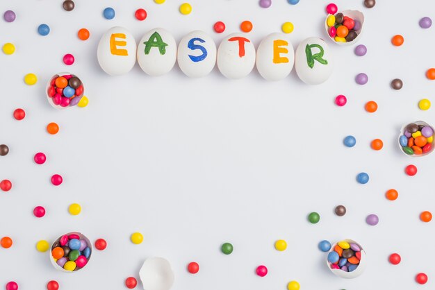 Inscripción de Pascua en huevos con caramelos en mesa blanca