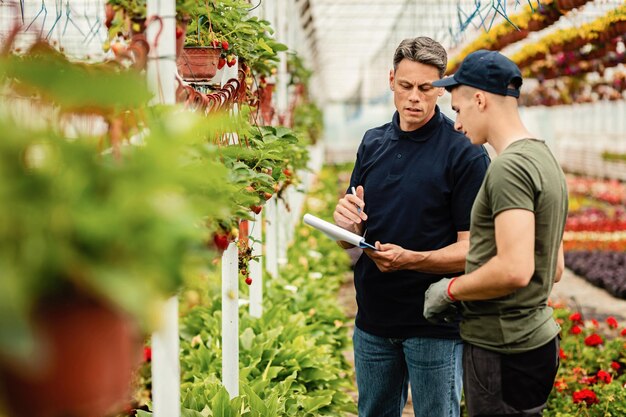 Inspector de control de calidad y trabajador hablando mientras revisa la lista de plantas en un invernadero