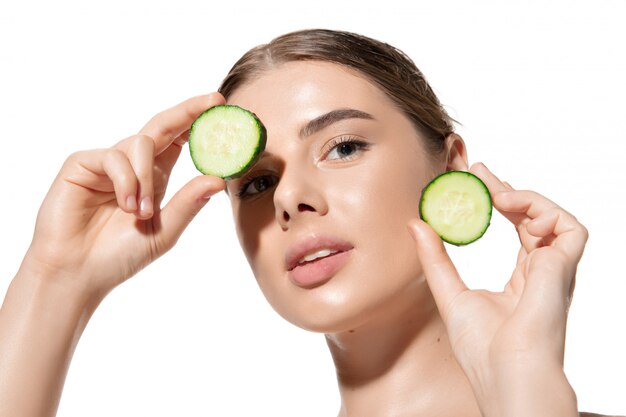 Inspirado. Ciérrese para arriba de mujer joven hermosa con las hojas verdes en su cara sobre blanco. Cosmética y maquillaje, tratamiento natural y ecológico, cuidado de la piel.