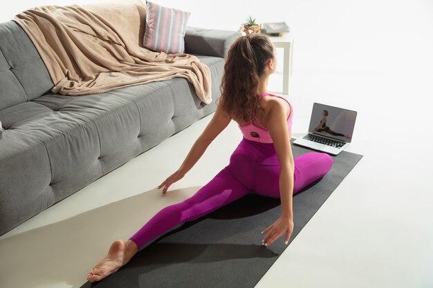 Inspirado. Hermosa joven trabajando en el interior, haciendo ejercicios de yoga en la alfombra gris en casa. Cabello largo en forma de modelo caucásico practicando. Concepto de estilo de vida saludable, mental, atención plena, equilibrio.