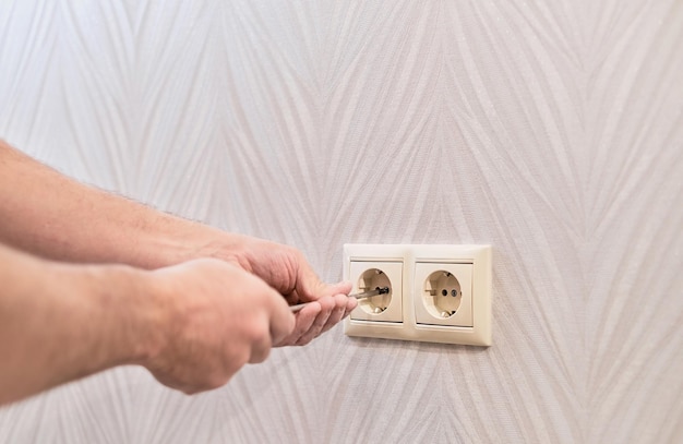 Instalación de enchufes en un apartamento nuevo Primer plano en manos de un electricista caucásico que sostiene un destornillador trabajando en el enchufe eléctrico en el sistema eléctrico residencial