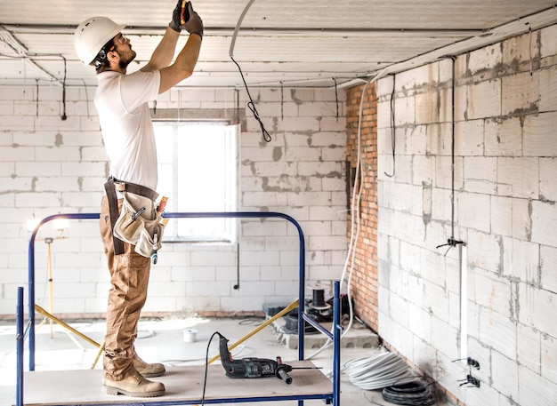 Instalador electricista con una herramienta en sus manos, trabajando con cable en el sitio de construcción