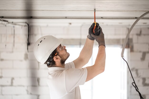 Instalador electricista con una herramienta en sus manos, trabajando con cable en el sitio de construcción.