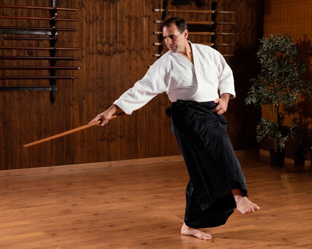 Instructor de artes marciales masculino con palo de madera en la sala de prácticas