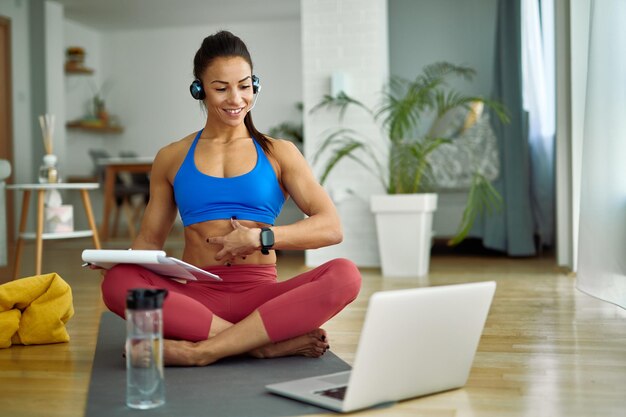 Instructor de fitness feliz asesorando a sus clientes sobre ejercicios abdominales mientras usa una computadora portátil en casa