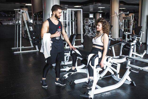 Instructor de fitness guapo está ayudando a su cliente atractivo a trabajar en un ejercicio en el gimnasio