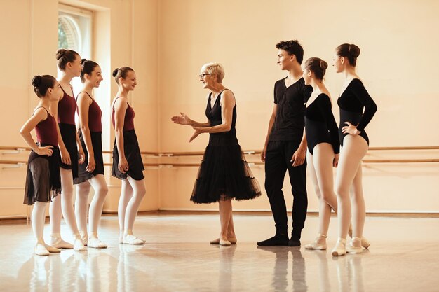 Instructora de ballet femenina feliz comunicándose con un grupo de bailarinas de ballet antes del ensayo en el estudio de baile