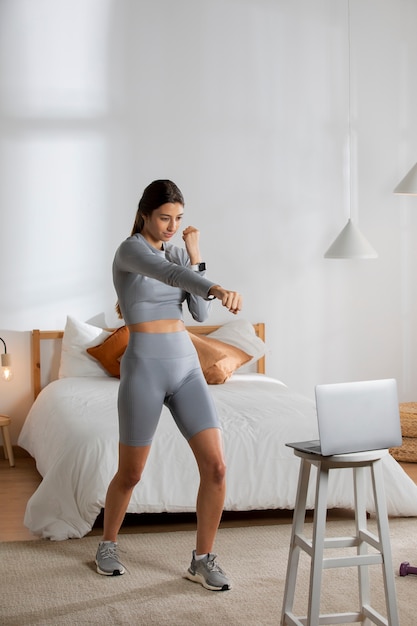 Instructora de fitness femenina enseñando una clase en casa frente a la computadora portátil