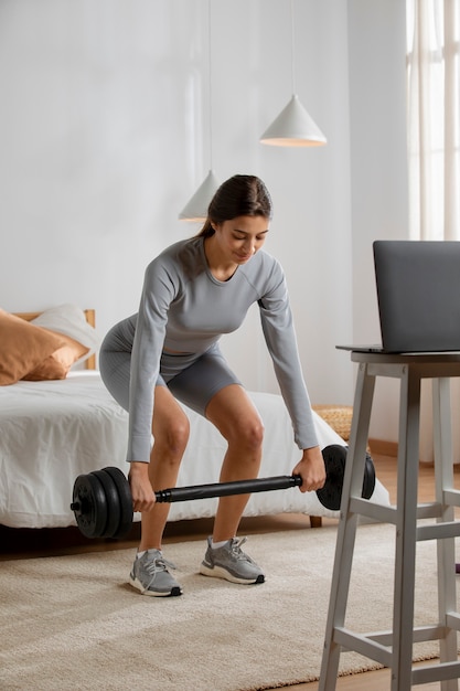 Instructora de fitness femenina levantando pesas en casa frente a la computadora portátil