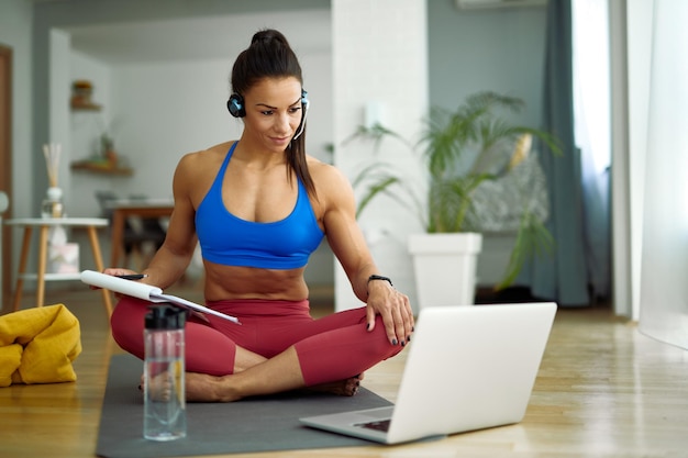 Instructora de fitness femenina que tiene consultas en línea mientras usa la computadora en la sala de estar