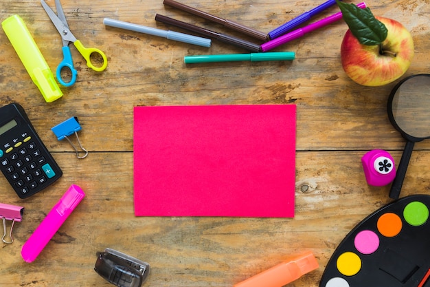 Instrumentos de escritura y manzana en círculo con nota adhesiva en el medio