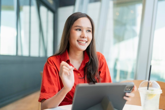 Inteligente, atractiva, mujer asiática, ropa casual, trabajo independiente, ocio, relajarse, trabajar con una computadora portátil y un teléfono inteligente en un café, un restaurante, un estilo de vida urbano, un nómada digital que trabaja en un espacio de trabajo compartido.