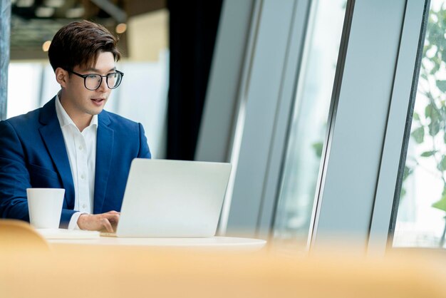 Inteligente, atractivo, positivo, hombre de negocios asiático, con gafas, trabajo remoto, nuevo estilo de vida normal, uso manual, portátil, teleconferencia, videollamada en vivo, reunión, concepto de ideas de negocios remotos.