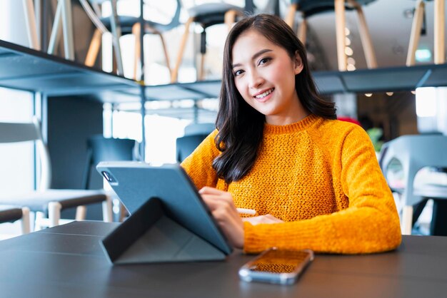 Inteligente casual empresaria asiática empresa de inicio empresaria propietario de una pequeña empresa trabajo y discusión con el cliente en el fondo de la oficina de la tienda nueva Atractiva mujer alegre uso tableta teléfono inteligente