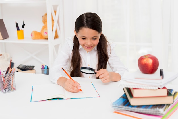 Foto gratuita inteligente colegiala hispana leyendo a través de la lupa.