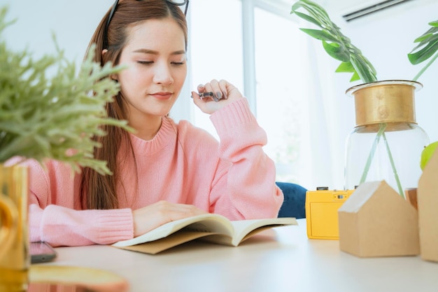 Inteligente hermosa mujer asiática casual disfruta leyendo el fin de semana del libro en el fondo de la casa de suéter rosa