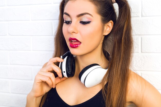 Interior de cerca retrato de moda de mujer hermosa joven, con maquillaje y peinado de moda brillante, escuchando música en auriculares, retrato urbano brillante de chica sexy dj