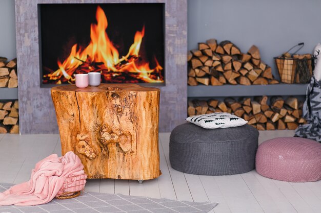 Interior escandinavo con una chimenea, mesa de tocón, una pila de troncos para el fuego