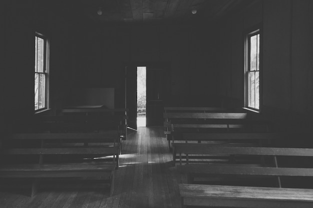 Un interior de una pequeña iglesia en el campo con bancos de madera y una puerta abierta.