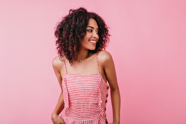 En el interior retrato de chica atractiva feliz con sonrisa blanca como la nieve. Mujer en vestido rosa de verano posando para sesión de fotos.