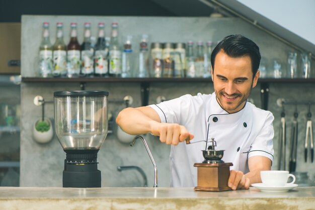 Interior tiro de joven macho barista haciendo una taza de café mientras está de pie detrás del mostrador de café. Joven verter la leche en una taza de café.