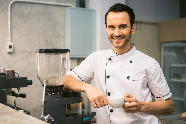 Foto gratuita interior tiro de joven macho barista haciendo una taza de café mientras está de pie detrás del mostrador de café. joven verter la leche en una taza de café. imagen filtrada vintage.