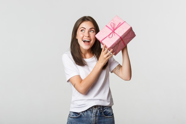 Intrigada niña feliz cumpleaños agitando caja de regalo para averiguar qué hay dentro.