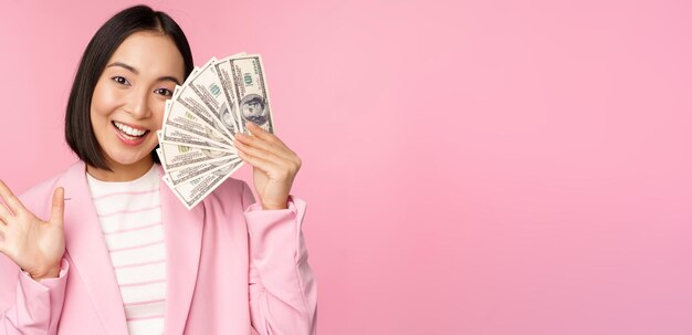 Inversión en microcrédito y concepto de gente de negocios Joven empresaria asiática dama corporativa mostrando dinero en efectivo dólares agitando la mano fondo rosa