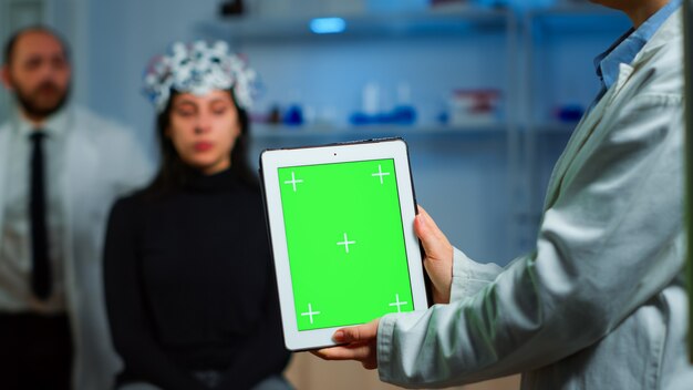 Investigador de atención médica sosteniendo y mirando tableta con pantalla chroma key en laboratorio neurológico. Equipo de científicos que realizan lectura de investigación médica en un dispositivo con pantalla verde, pantalla de maqueta aislada