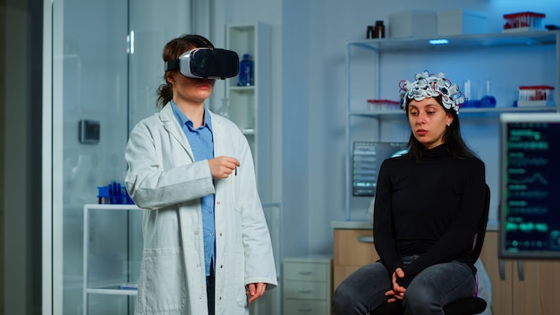 Investigador profesional con gafas de realidad virtual utilizando innovación médica en el laboratorio que analiza el escáner cerebral del paciente. Equipo de médicos neurológicos que trabajan con equipo, dispositivo simulador de alta tecnología.