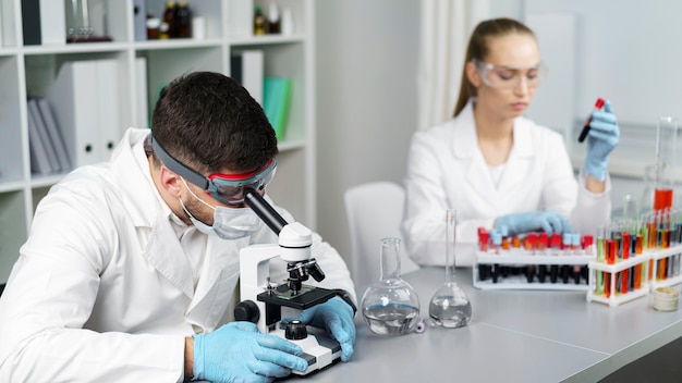 Investigadora y colega en el laboratorio con tubos de ensayo y gafas de seguridad