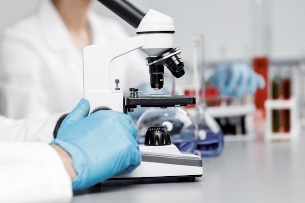 Investigadora con guantes y microscopio en el laboratorio.