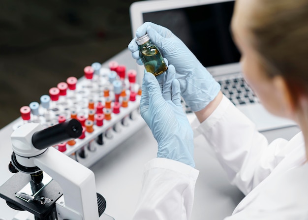 Investigadora en el laboratorio con tubos de ensayo y botella de vacuna