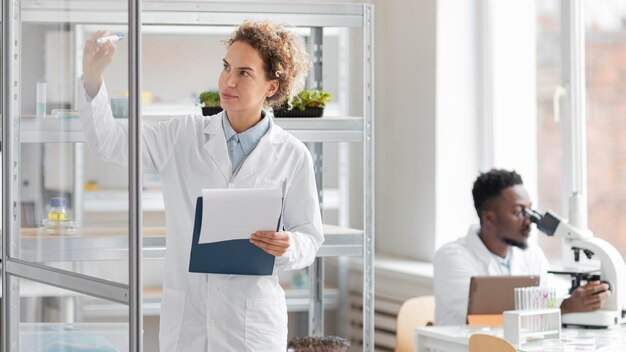 Investigadora con portapapeles en el laboratorio de biotecnología y colega masculino