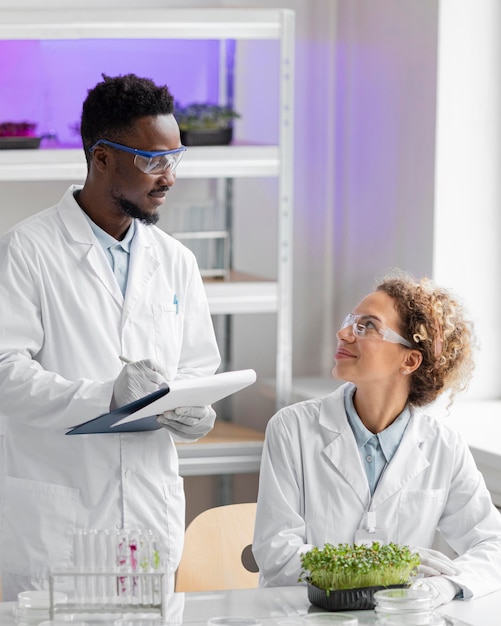 Investigadores sonrientes en el laboratorio comprobando la planta y escribiendo en el portapapeles