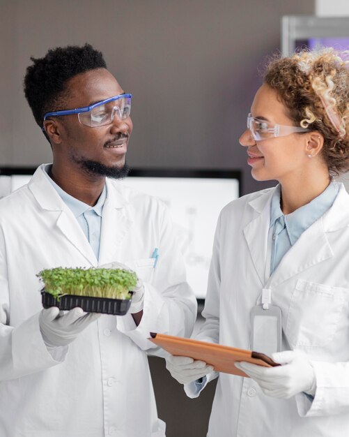 Investigadores sonrientes en el laboratorio con gafas de seguridad y planta