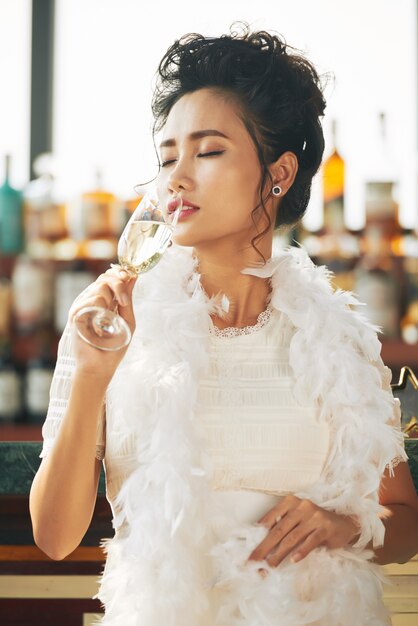 Invitada asiática disfrutando de copa de champán en la fiesta en el bar