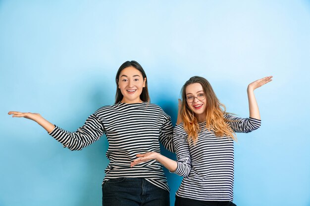 Invitando, saludando. Mujeres emocionales jóvenes aisladas en la pared azul degradado. Concepto de emociones humanas, expresión facial, amistad, anuncio. Hermosas modelos caucásicas en ropa casual.