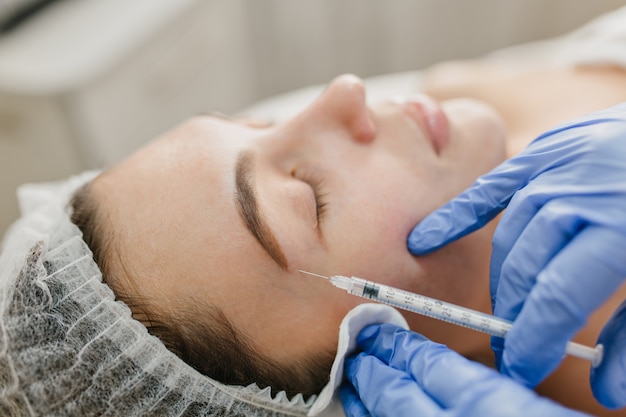 Inyección de retrato de primer plano en la cara de una mujer bonita durante los procedimientos de botox en el salón. Trabajo profesional, manos en guantes azules, médico, rejuvenecimiento, medicina moderna, belleza, cuidado de la salud