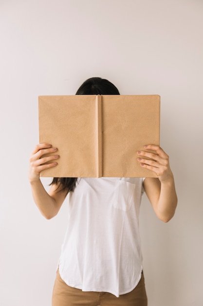 Irreconocible libro de lectura de la señora cerca de la pared blanca