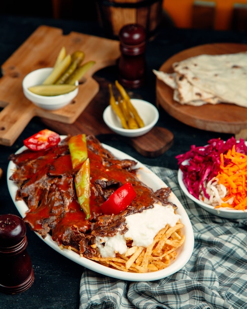 Iskender kebab adornado con salsa de tomate, servido con papa y yogurt