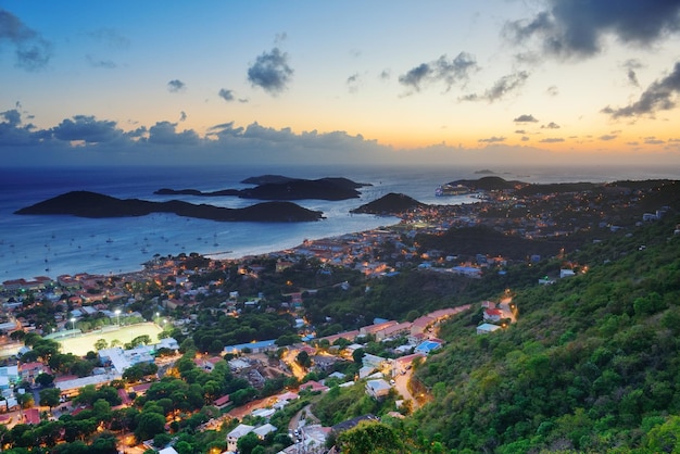 Islas Vírgenes Santo Tomás puesta de sol vista a la montaña con nubes coloridas, edificios y costa de playa.