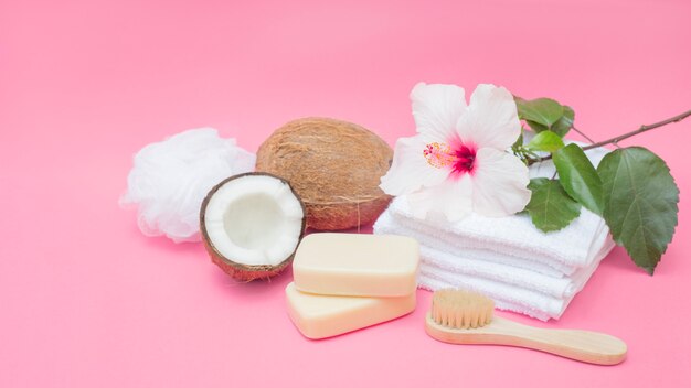 Jabón; cepillo; Coco; esponja; flores y toallas sobre fondo rosa