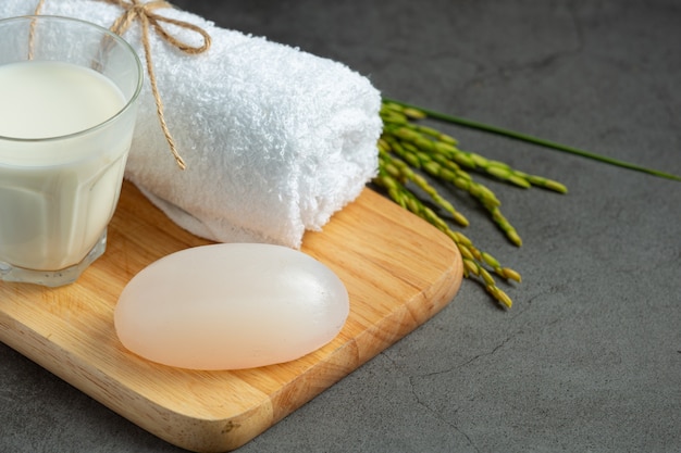 Jabón de leche de arroz, toalla enrollada, plantas de arroz y vaso de leche en prueba de madera