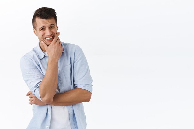 Jaja muy divertido Retrato de un chico guapo y elegante que se ríe de algo hilarante tocando la mandíbula limpia y afeitada y sonriendo complacido mirando la cámara satisfecha de fondo blanco