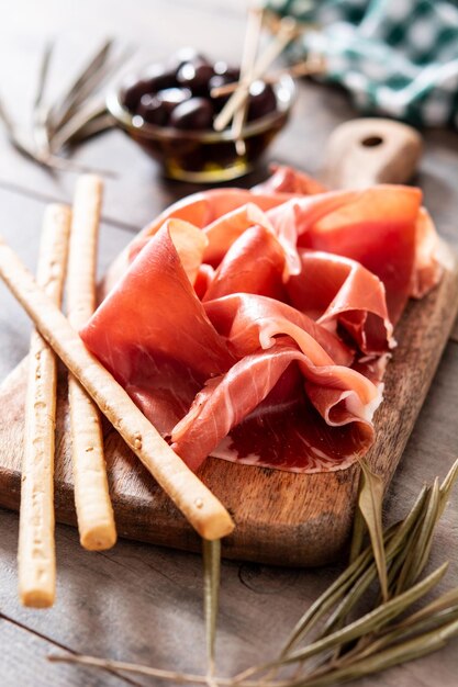 Jamón serrano español con aceitunas y palitos de pan sobre fondo de mesa de madera